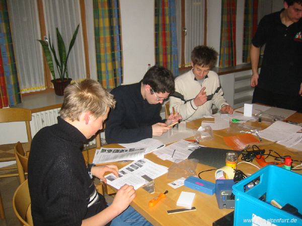 Teilnehmer des Workshops sitzen an einem Tisch, vor ihnen diverses Bastelmaterial