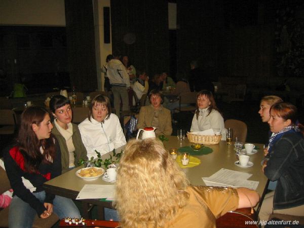 Mehrere Mädchen und junge Frauen sitzen um einen Tisch und singen