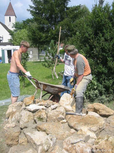 Zwei junge Männer errichten zusammen mit Herrn Bachmann aus Felsbrocken und Zement das Fundament für die Lourdes-Grotte