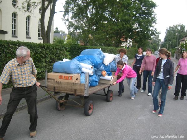 Einige Jugendliche schieben einen großen Handwagen, der mit Kisten aus dem Kindergarten beladen ist