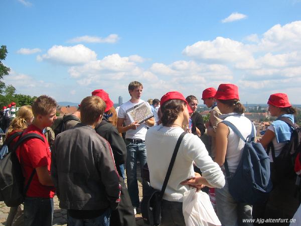 Ein Fremdenführer zeigt anhand einer Zeichnung, wie die Stadtmauer im Mittelalter ausgesehen hat. Alle Teilnehmer haben beim Start rote Sonnenhüte erhalten