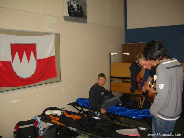 Ein Klassenzimmer in der Schule des Klosters Calvarienberg in Ahrweiler. Mehrere Jugendliche stehen zwischen Schlafsäcken und Feldbetten, einer von ihnen spielt Gitarre. An der Wand hängt eine rot-weiße Frankenflagge