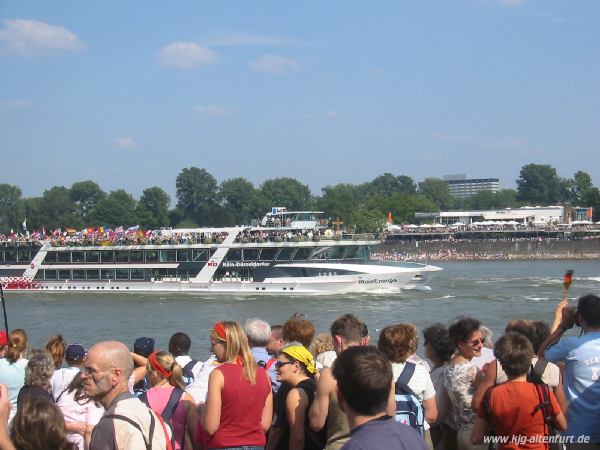 Ein Personenschiff auf dem Rhein. Auf dem Vorderdeck steht das Weltjugendtagskreuz und die Marienikone, auf dem Oberdeck stehen Pilger aus allen Ländern mit ihren Fahnen