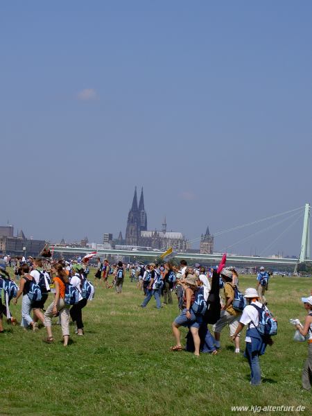 Jugendliche, die über eine Wiese zum Rhein laufen, im Hintergrund der Kölner Dom