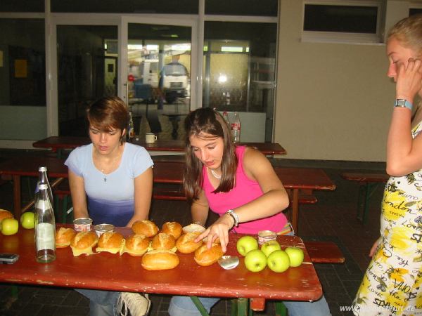 Steffi und Lisa machen Lunch-Pakete. Vor ihnen liegen bereits elf Semmeln, 7 Äpfel und mehrer Dosen Wurst