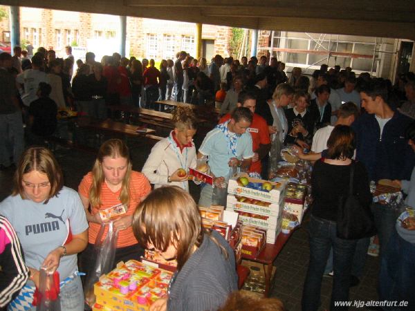 Die Jugendlichen stehen in einer langen Schlange an und packen an den verschieden Tischen Vorräte für die nächten Tage ein