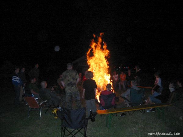 Lagerfeuer, die Teilnehmer und Leiter sitzen auf Bierbänke im Kreis darum