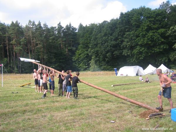 Elf Teilnehmer und Gruppenleiter versuchen den 16 Meter lanegn Fahnenmast aufzustellen