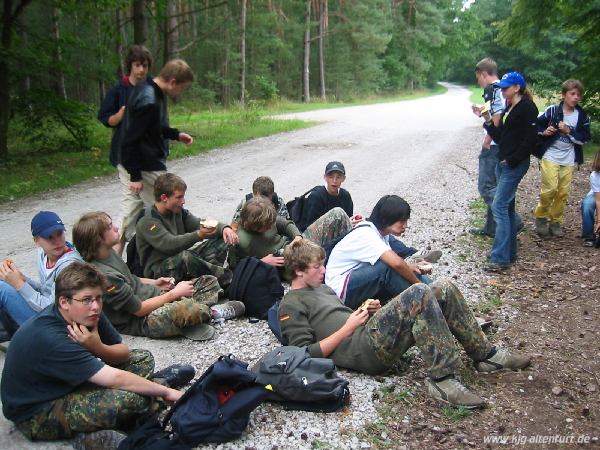 Die älteren Teilnehmer sitzen (mehrheitlich in Tarnkleidung) auf dem Boden und vespern