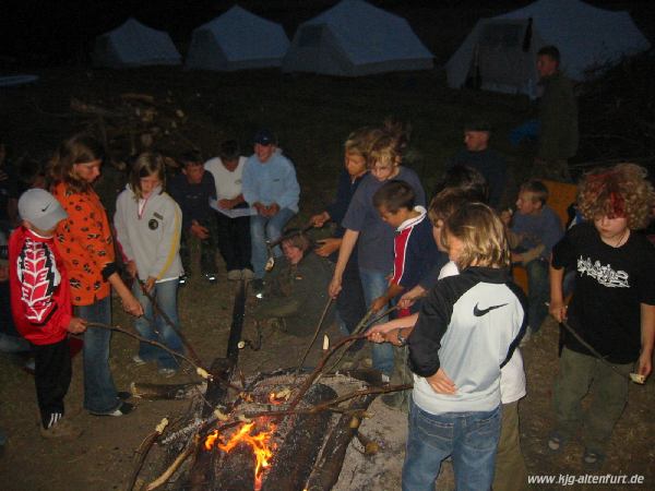 Die Teilnehmer halten Stöcke mit Brotteig über das Lagerfeuer