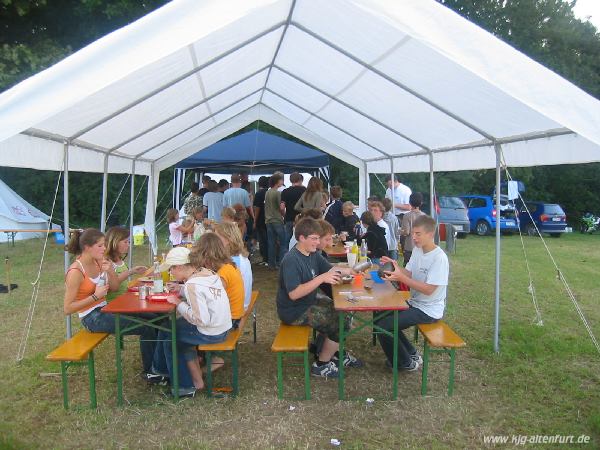 Die Teilnehmer sitzen auf Biertisch-Garnituren unter dem großen Pavillon und essen