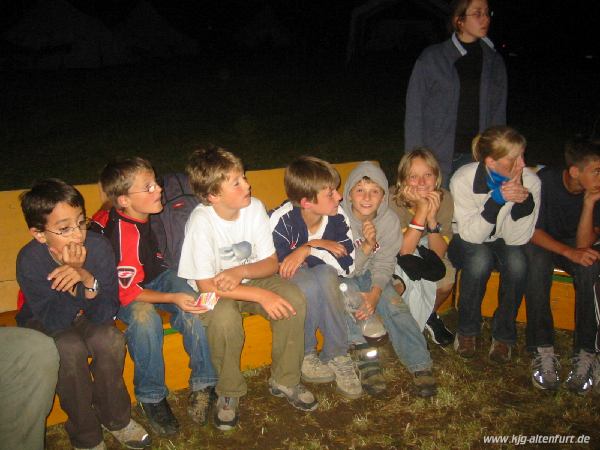 Teilnehmer und Leiter sitzen auf Bierbank-Sofas um das Lagerfeuer