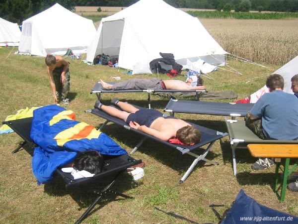 Vor dem Zelt der großen Jung stehen mehrere Feldbetten, auf denen sie ihren Mittagsschlaf halten