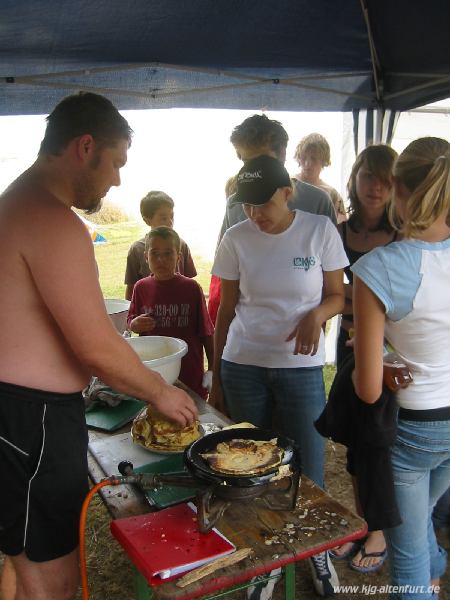 Eine Gruppe bäckt Pfannkuchen, als Pfanne dient ein umgedrehter Topfdeckel über dem Gaskocher