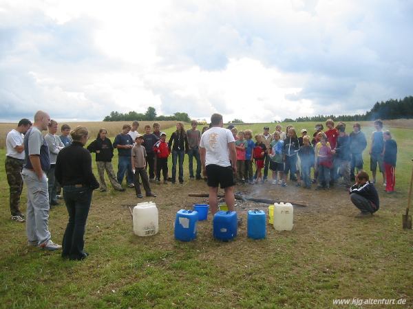 Alle Teilnehmer und Leiter stehen zu Reflexion um die Feuerstelle. Für alles was gut gefallen hat wird Wasser in den grünen Eimer gegossen, für das schlechte in den blauen