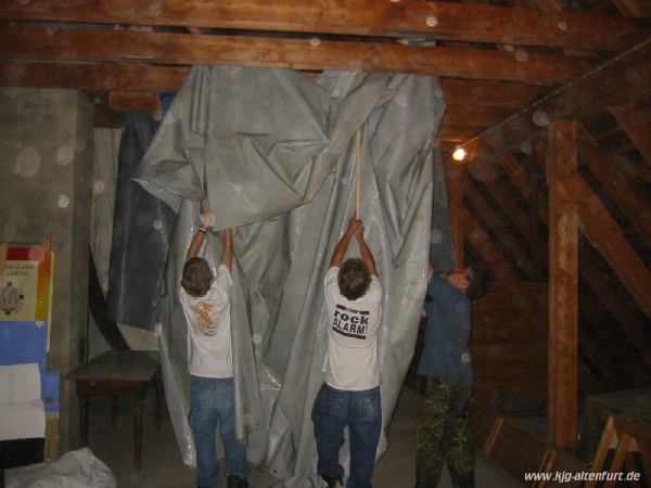 Drei Grüpplinge heben die Zeltböden mit Besenstielen auf die Balken im Pfarrdachboden, wo sie zum Trocknen aufgehängt werden