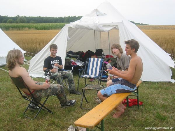 Vier Teilnehmer sitzen vor ihrem Zelt