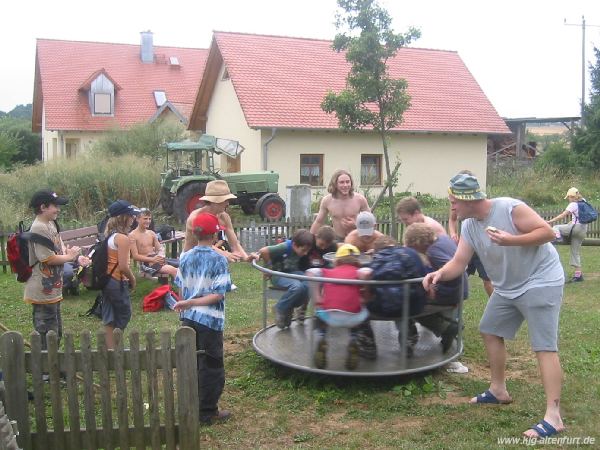 Mehrere Kinder sitzen auf einem Karusell und werden angeschubst