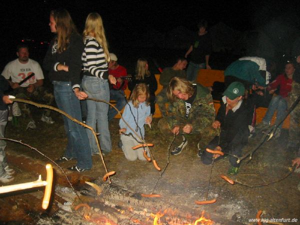 Auf Stecken werden Würstchen über das Lagerfeuer gehalten